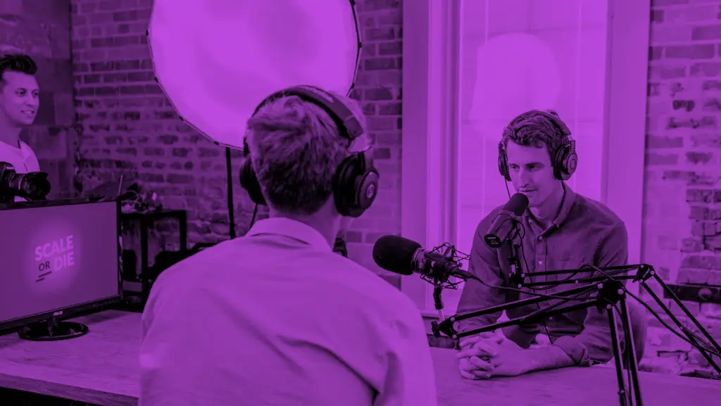 pitch please. – Der Startup Podcast für junge Gründer | Online Marketing und Social Media Agentur Zwei Menschen sitzen jeweils mit einem Mikrofon und Kopfhörern gegenüber an einem Tisch und unterhalten sich.